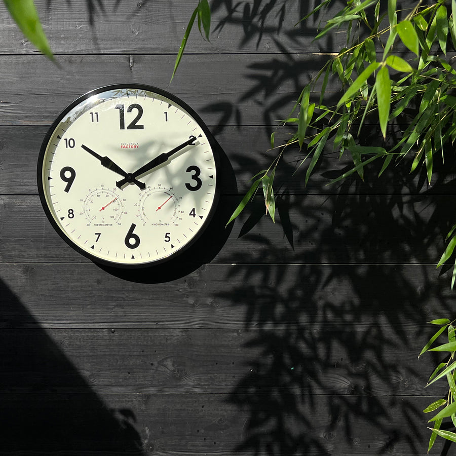 Outdoor Wanduhr schwarz aufgehängt neben Pflanzen